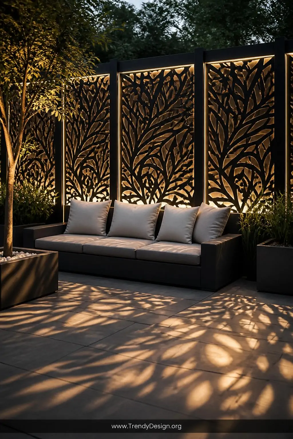 Wide shot of a dramatic backyard accent wall made of laser-cut geometric black metal fence panels backlit with warm white LED