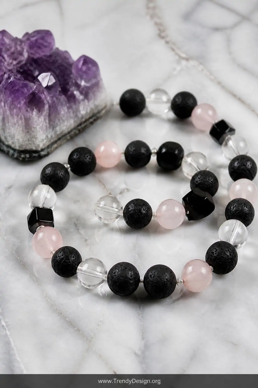 Closeup shot of a styled marble surface displaying a lava bead bracelet interspersed with clear quartz, rose quartz, and blac