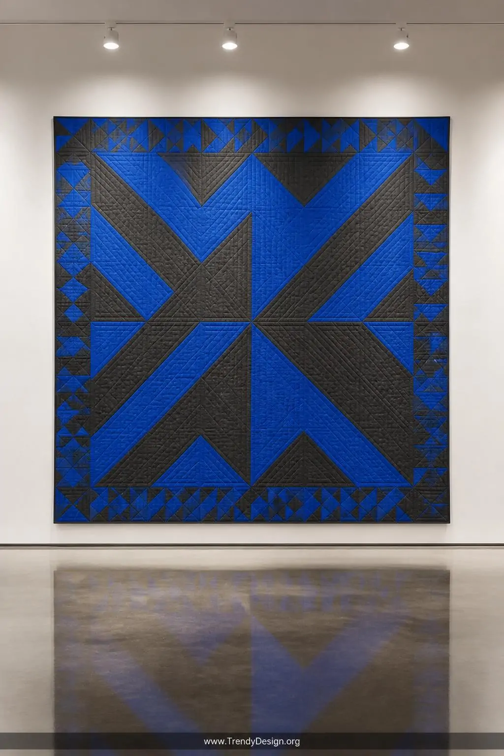 Wide shot of a bold graphic quilt hung flat on a white gallery wall in a modern interior, flying geese border showing alterna
