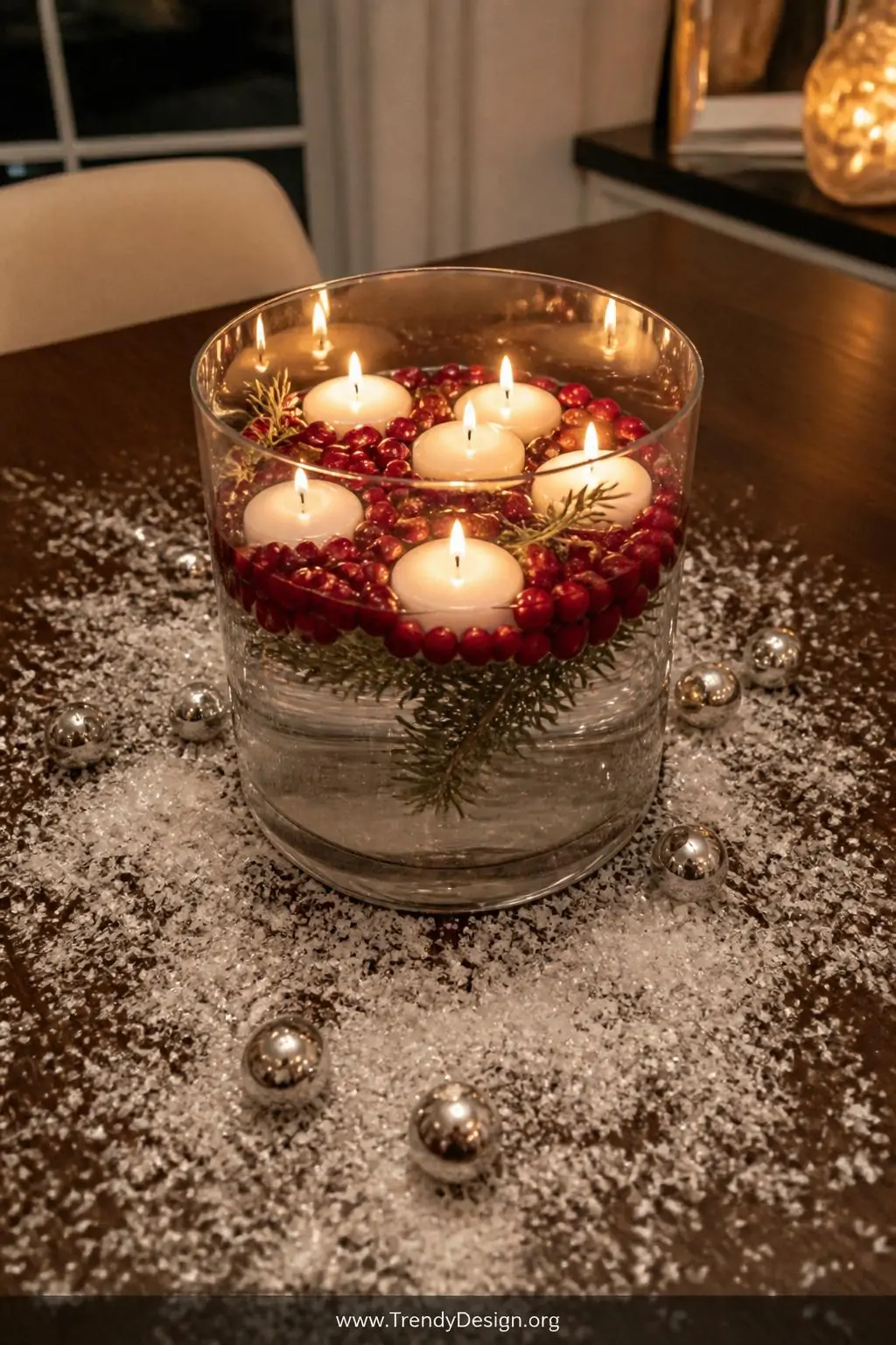 A close-up overhead shot of a large clear glass cylinder vase centerpiece on a dark walnut dining table, white pillar candles