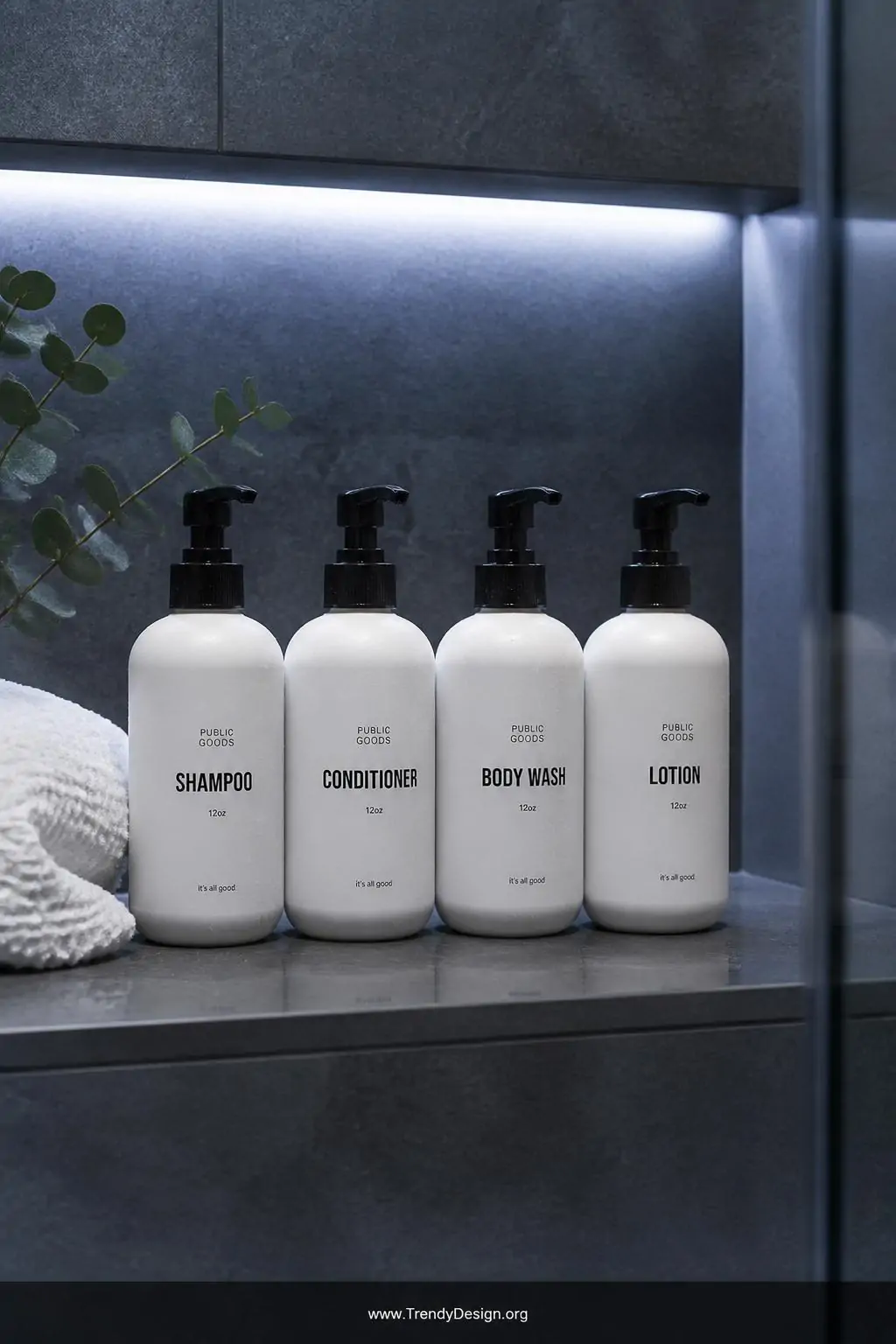 Medium shot of four matching frosted white pump bottles with clean minimalist black labels lined in a precise row on a wet-lo