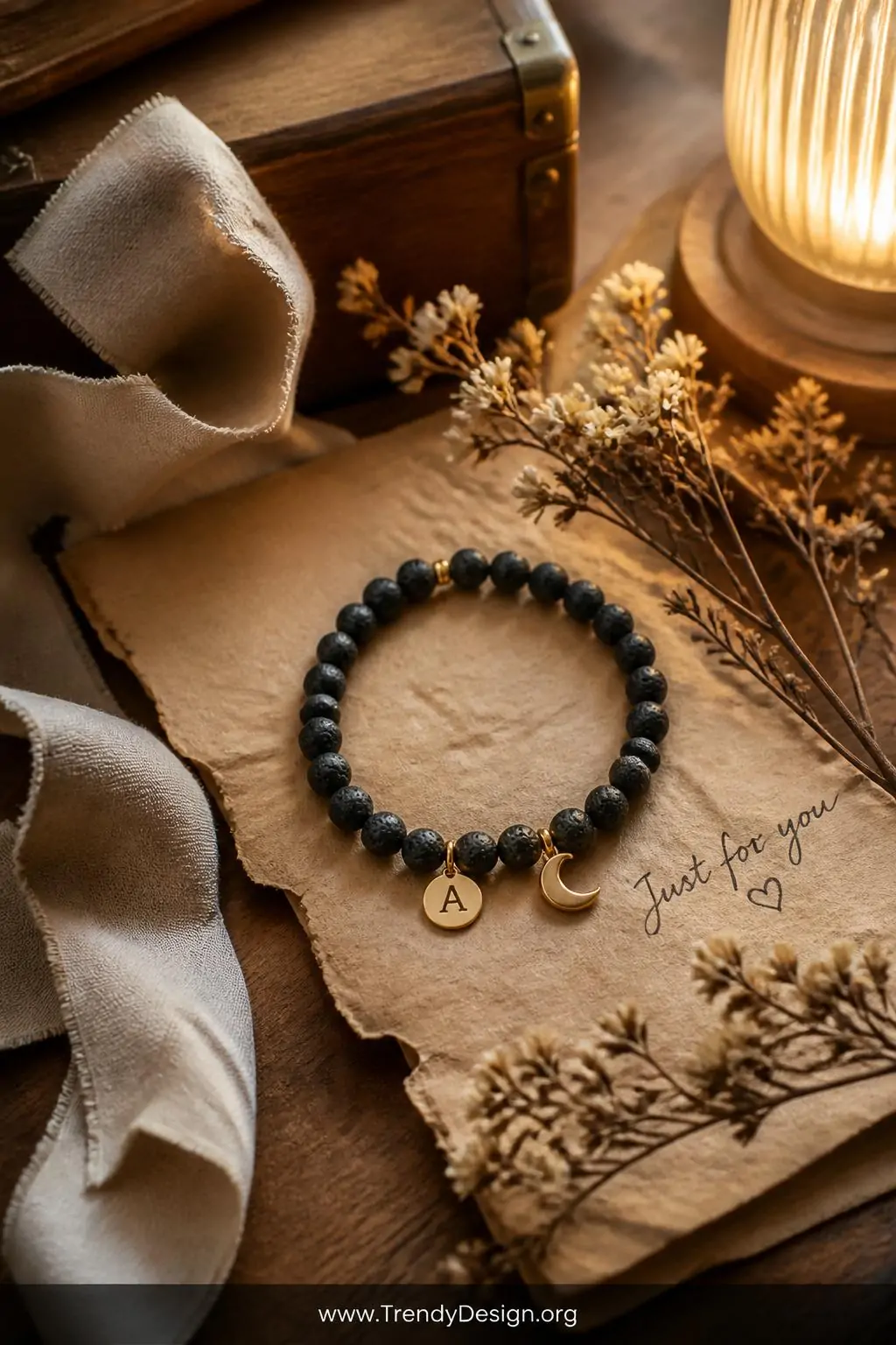 Medium shot of a warm rustic gift styling vignette featuring a personalized lava bead bracelet with a small gold initial char