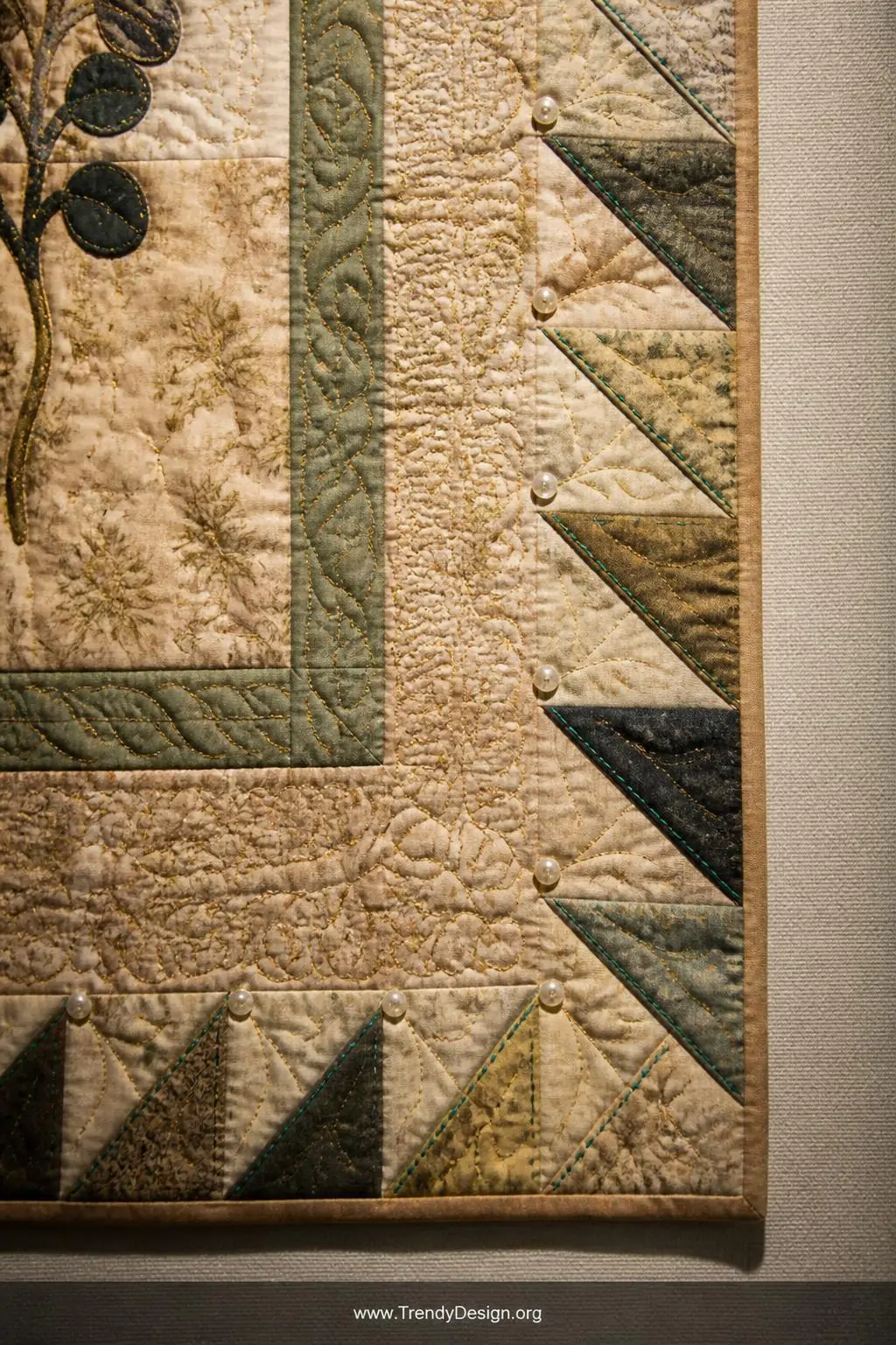 Closeup shot of an art quilt section displayed on a linen-covered exhibition surface, flying geese border units embellished w