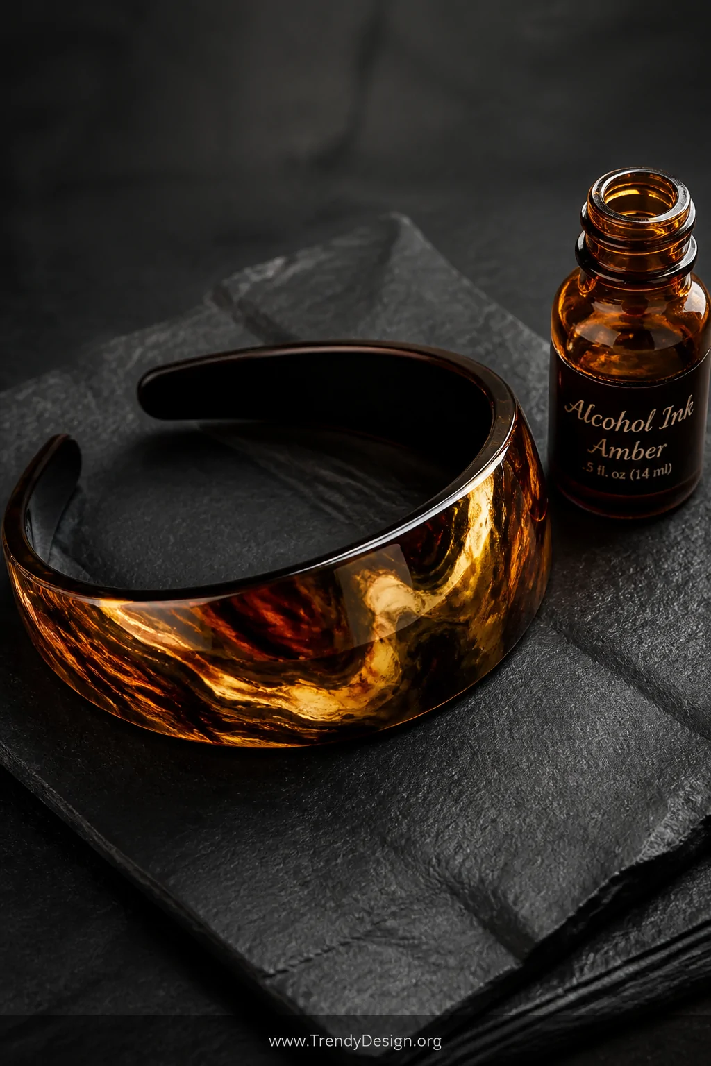 A closeup detail shot of a glossy resin headband with swirling amber, chocolate brown, and liquid gold tortoiseshell marbling