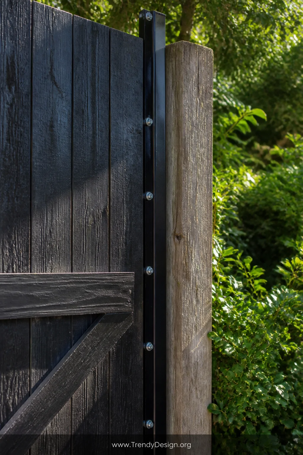 Medium shot of a galvanized steel angle iron bolted vertically along the edge of a weathered wooden fence gate, painted gloss