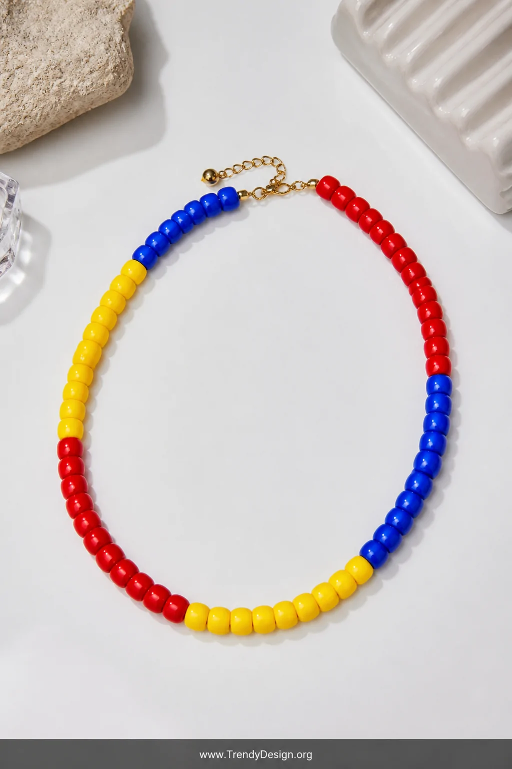 A medium flat-lay shot on a clean white lacquered surface displaying a color block pony bead necklace divided into bold graph