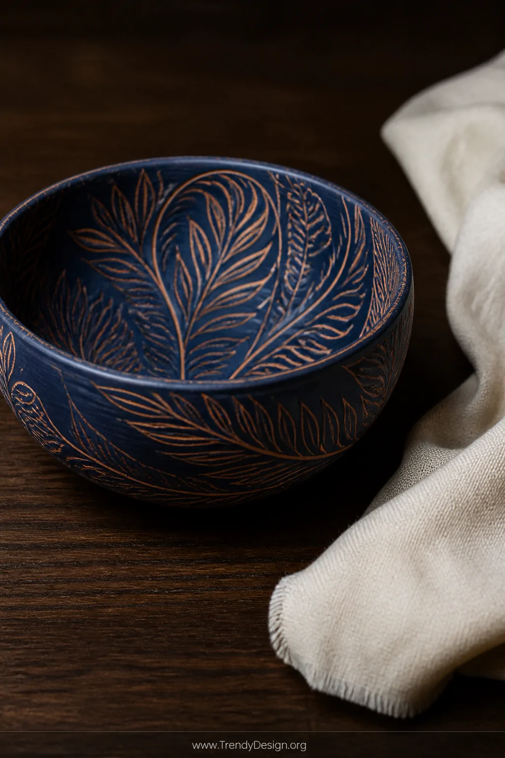 A closeup detail shot of a ceramic bowl featuring sgraffito technique with deep navy blue slip and warm terracotta carved des