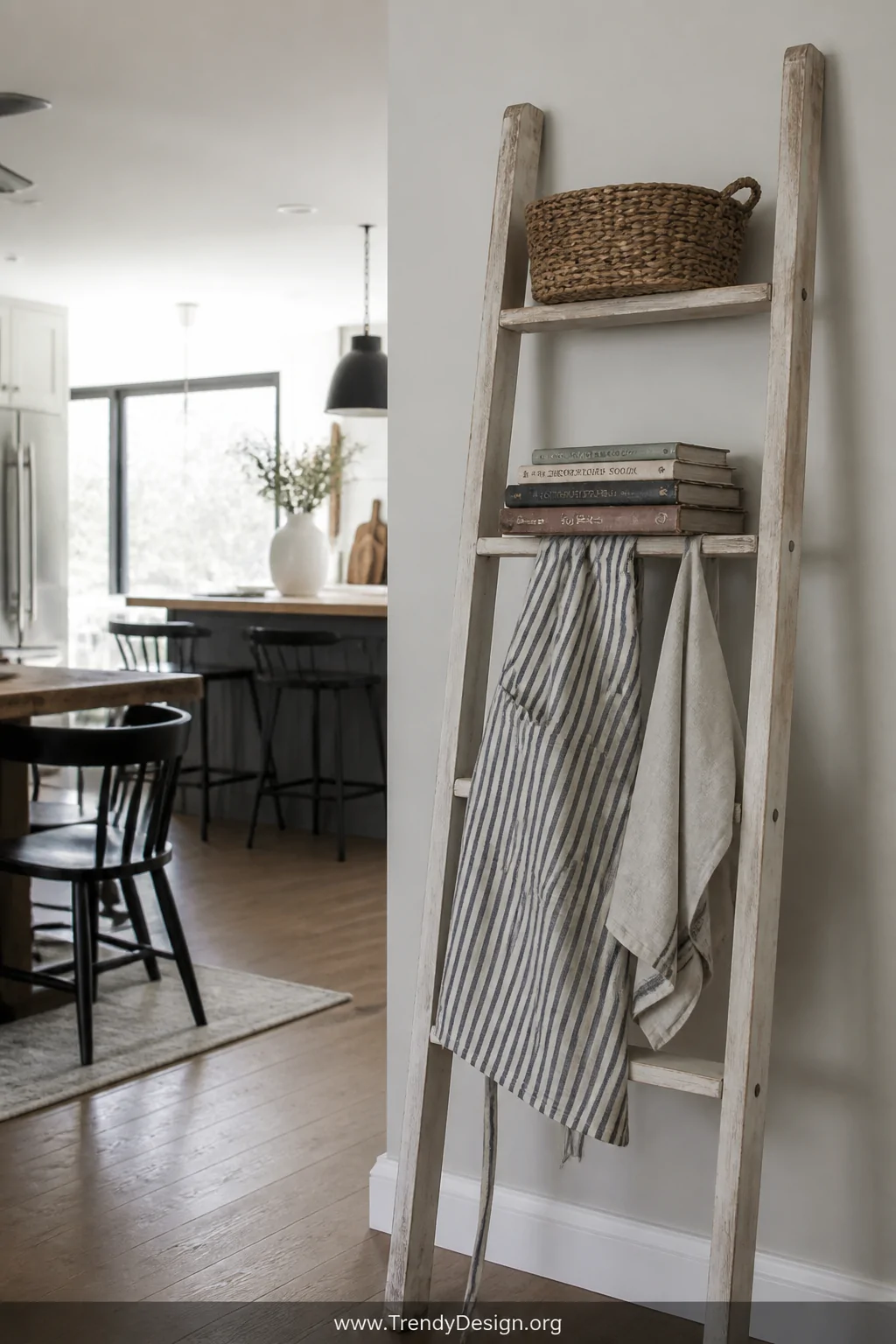 Medium shot of a whitewashed wood leaning ladder shelf propped against a light gray kitchen wall, a photogenic striped cotton