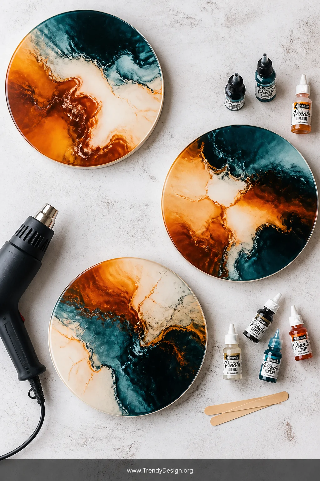 A medium overhead flat lay shot of three freshly poured circular resin art pieces cooling on a white concrete surface, each d