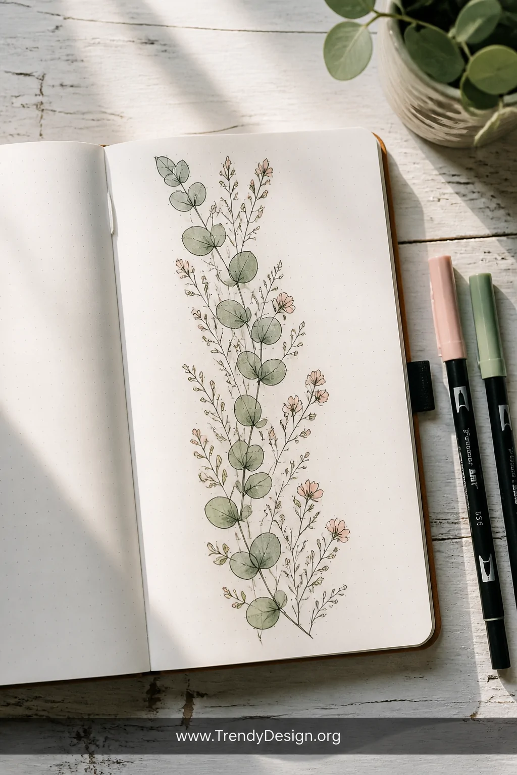 A medium overhead shot of an open journal spread on a weathered white wooden surface, displaying a hand-drawn botanical divid