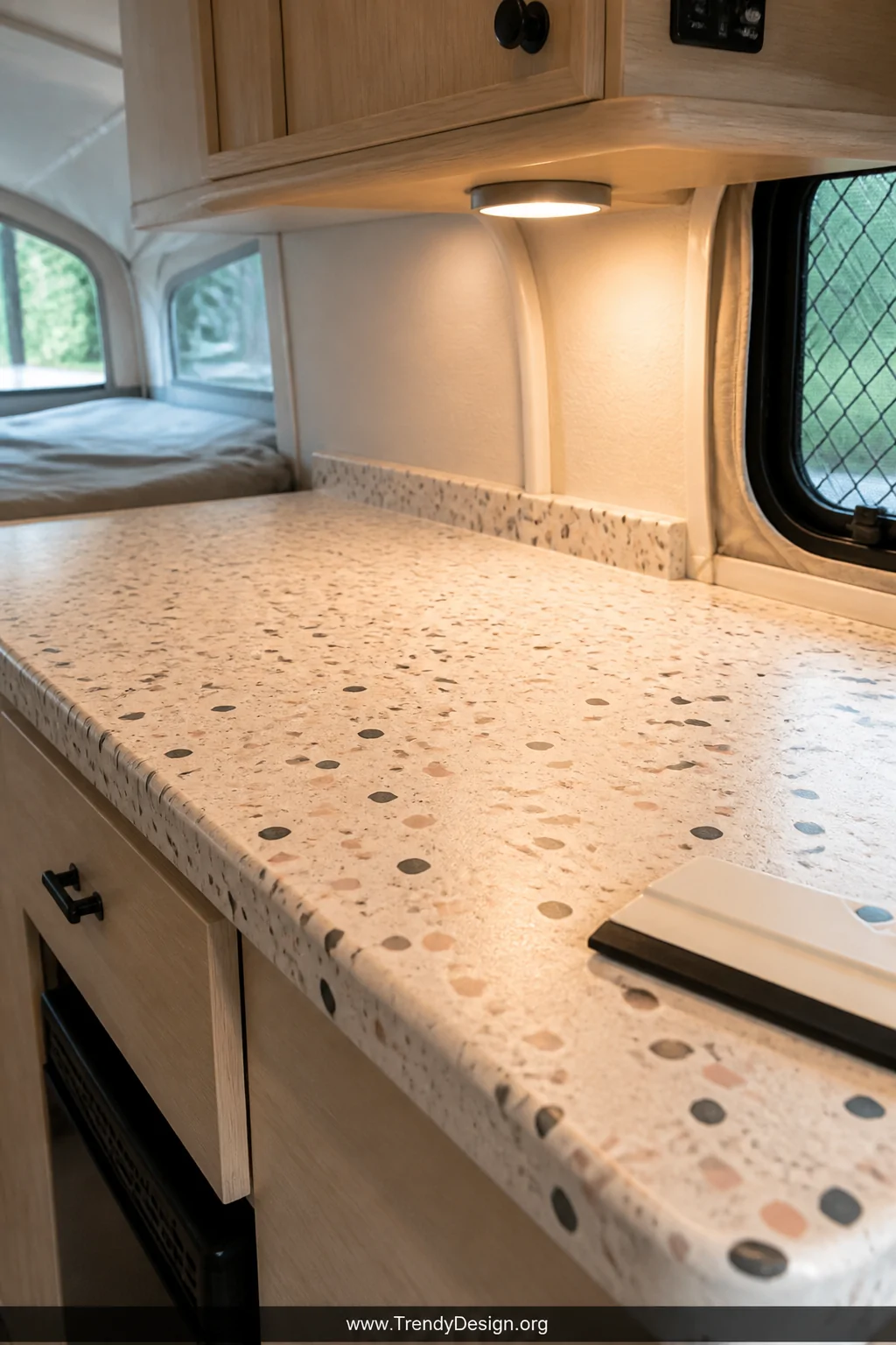 A close-up detail shot of a pop-up camper countertop freshly covered in realistic faux terrazzo contact paper in cream, blush