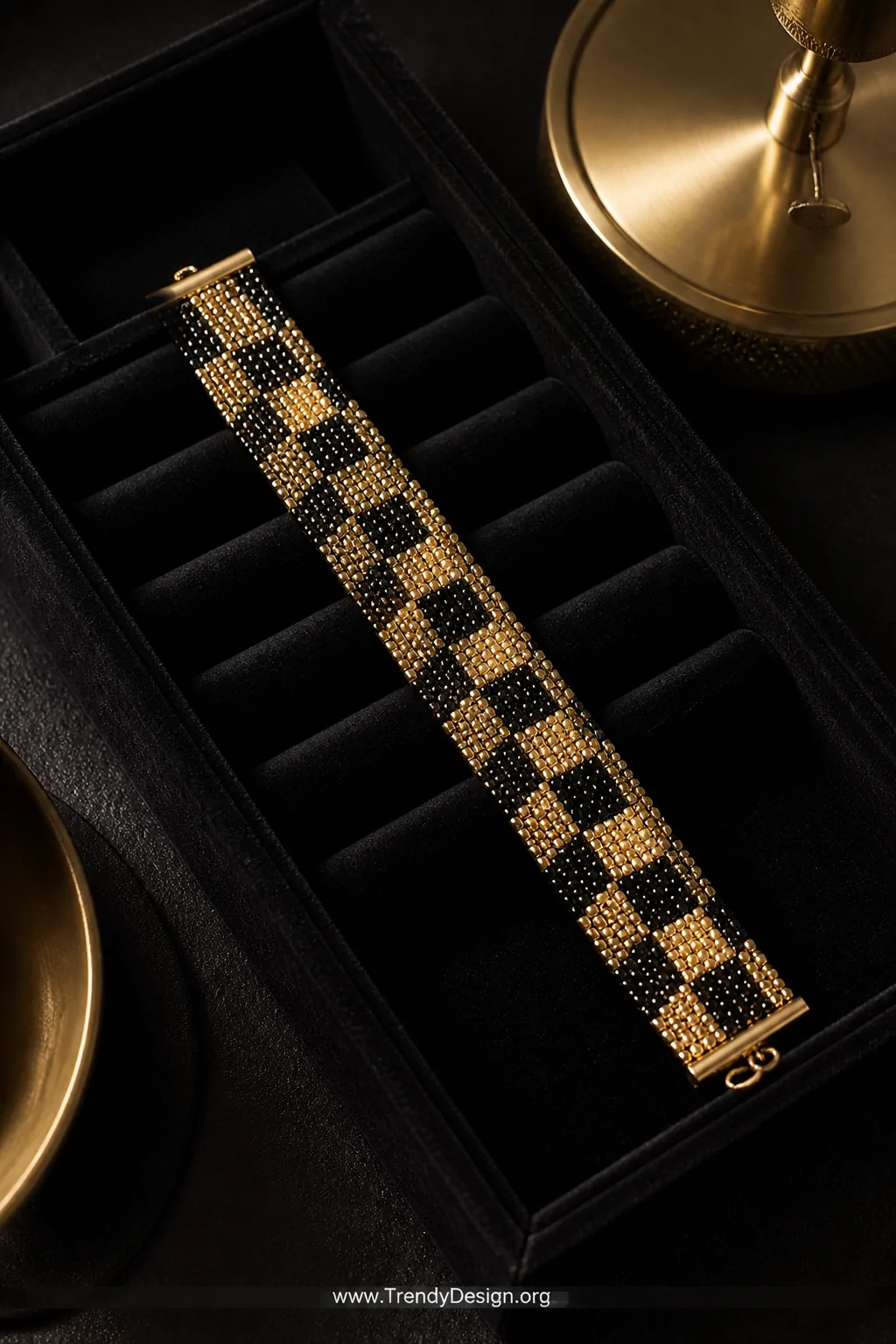 A closeup overhead shot of a black velvet jewelry tray holding a seed bead loom bracelet in a bold black and gold checkerboar