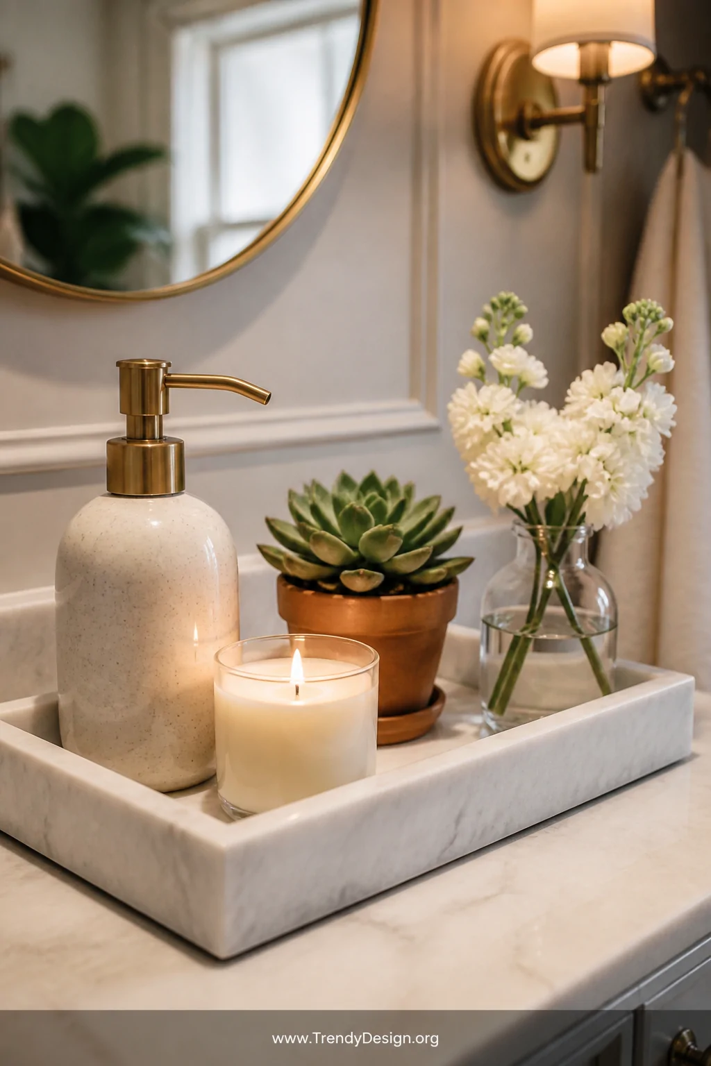 A close-up styled shot of a rectangular white marble vanity tray holding a ceramic hand soap dispenser, a small lit cream can