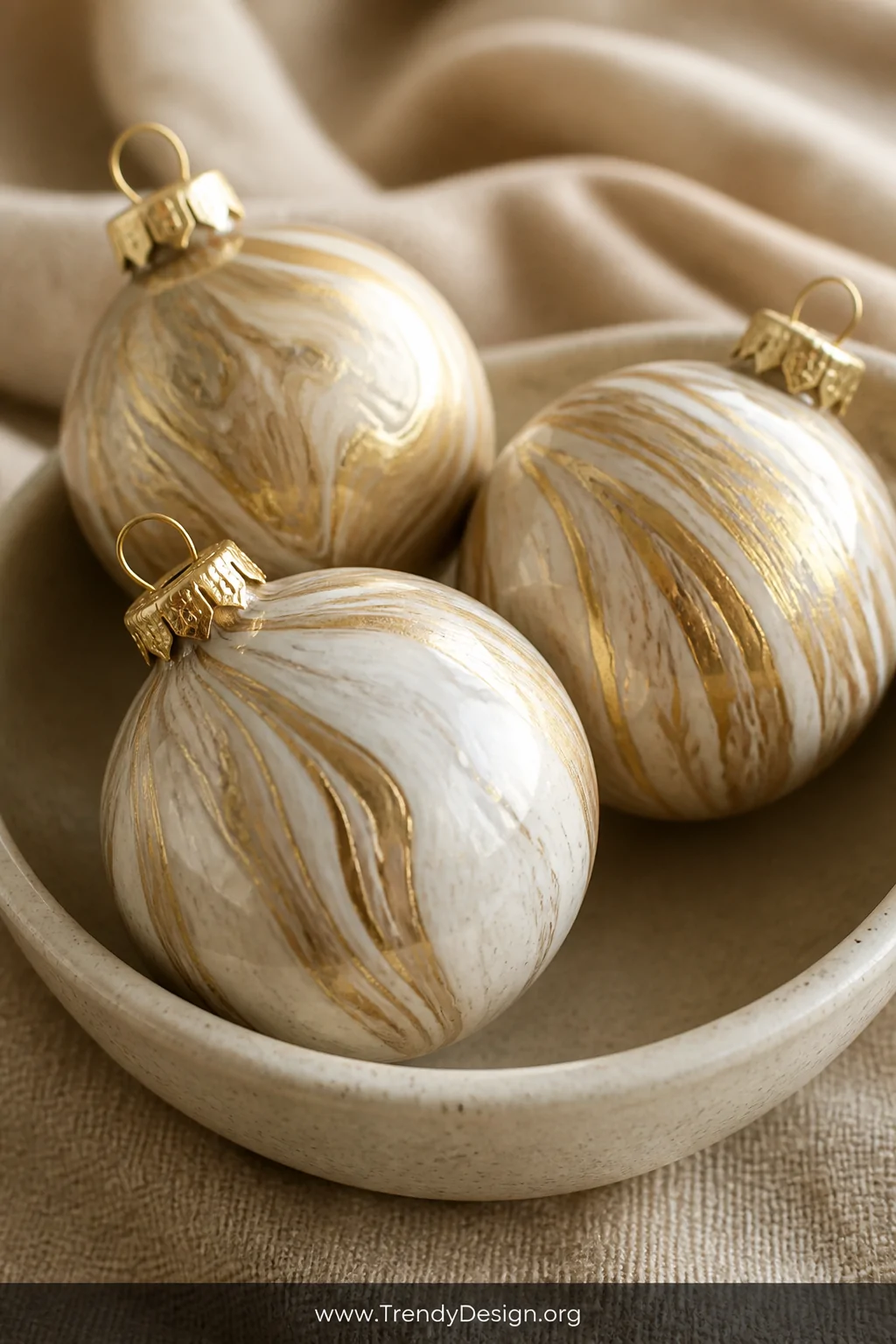 A close-up detail shot of three marble-effect Christmas ornaments resting in a shallow ceramic bowl, their surfaces swirled w