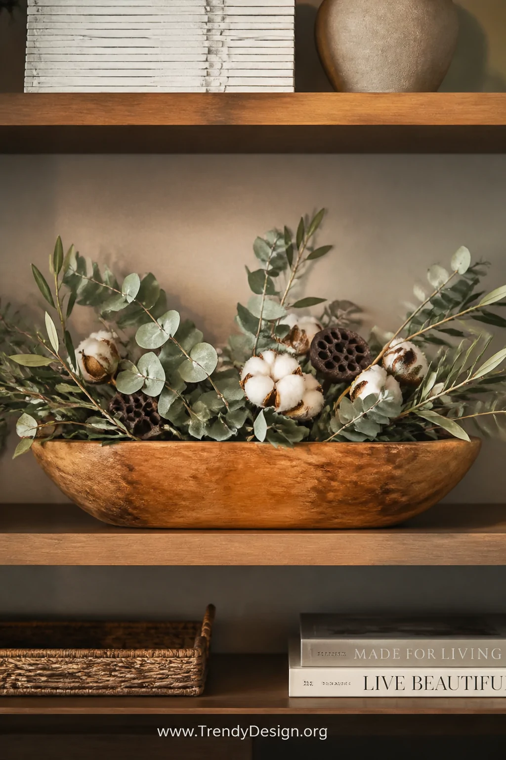 A medium shot of a wooden dough bowl on a styled open shelving unit filled with loosely arranged high-quality faux olive bran