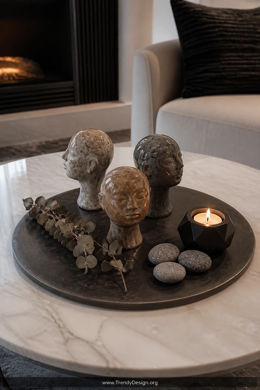 A medium overhead shot of a round marble coffee table featuring a dark slate tray styled with three mini clay head sculptures