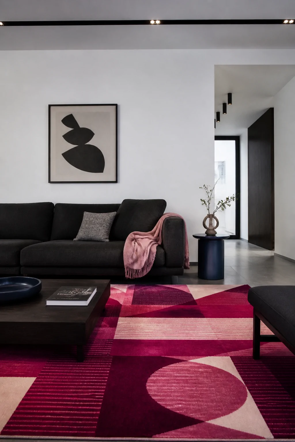 Medium shot of a bold magenta geometric-patterned statement rug anchoring a minimalist living room with stark white walls, a 