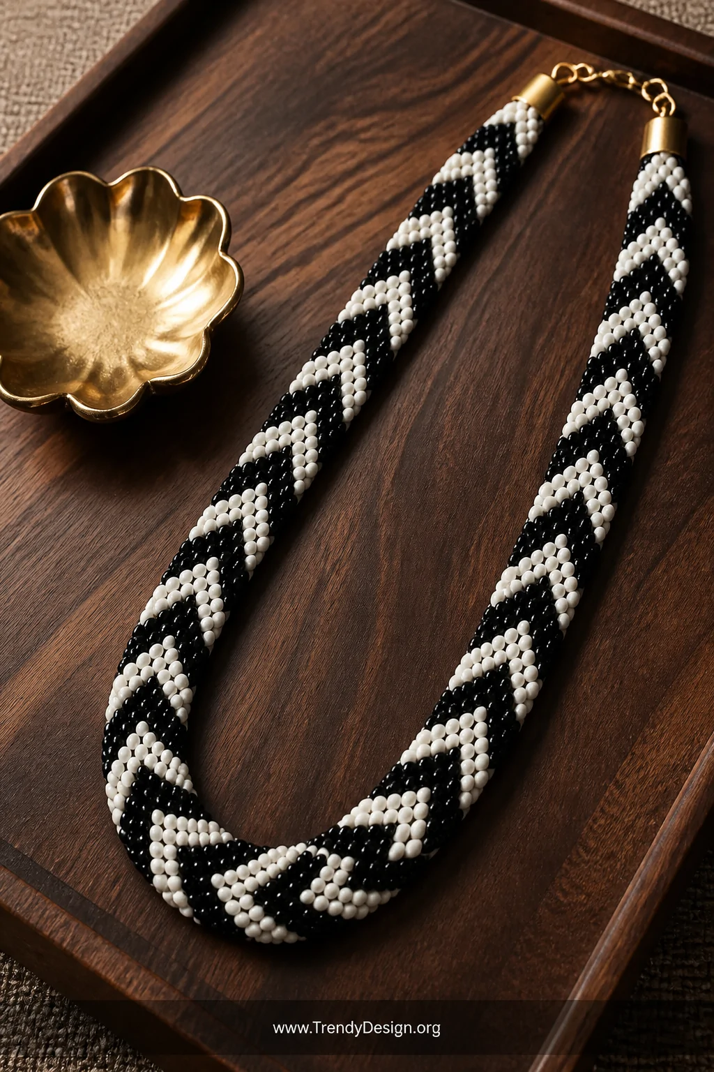 A medium close-up shot on a dark walnut wooden tray showing a chevron zigzag pony bead necklace in bold black and white with 