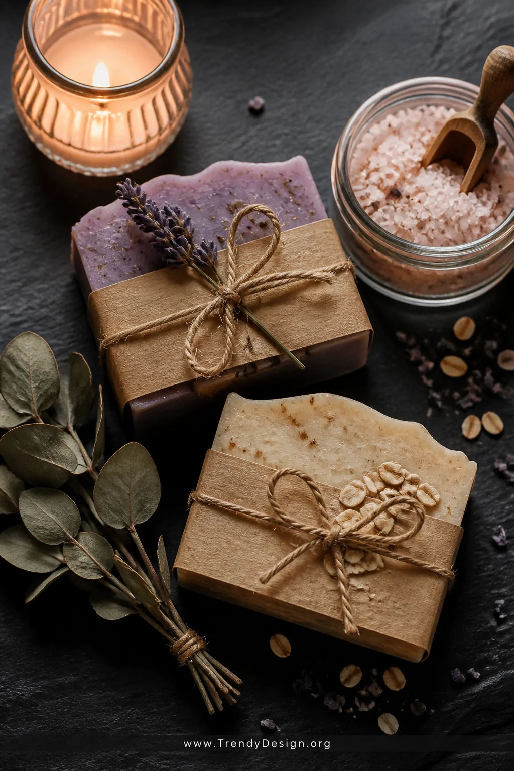 A styled product flat-lay on a dark slate surface showing handmade lavender and oatmeal soap bars wrapped in kraft paper with