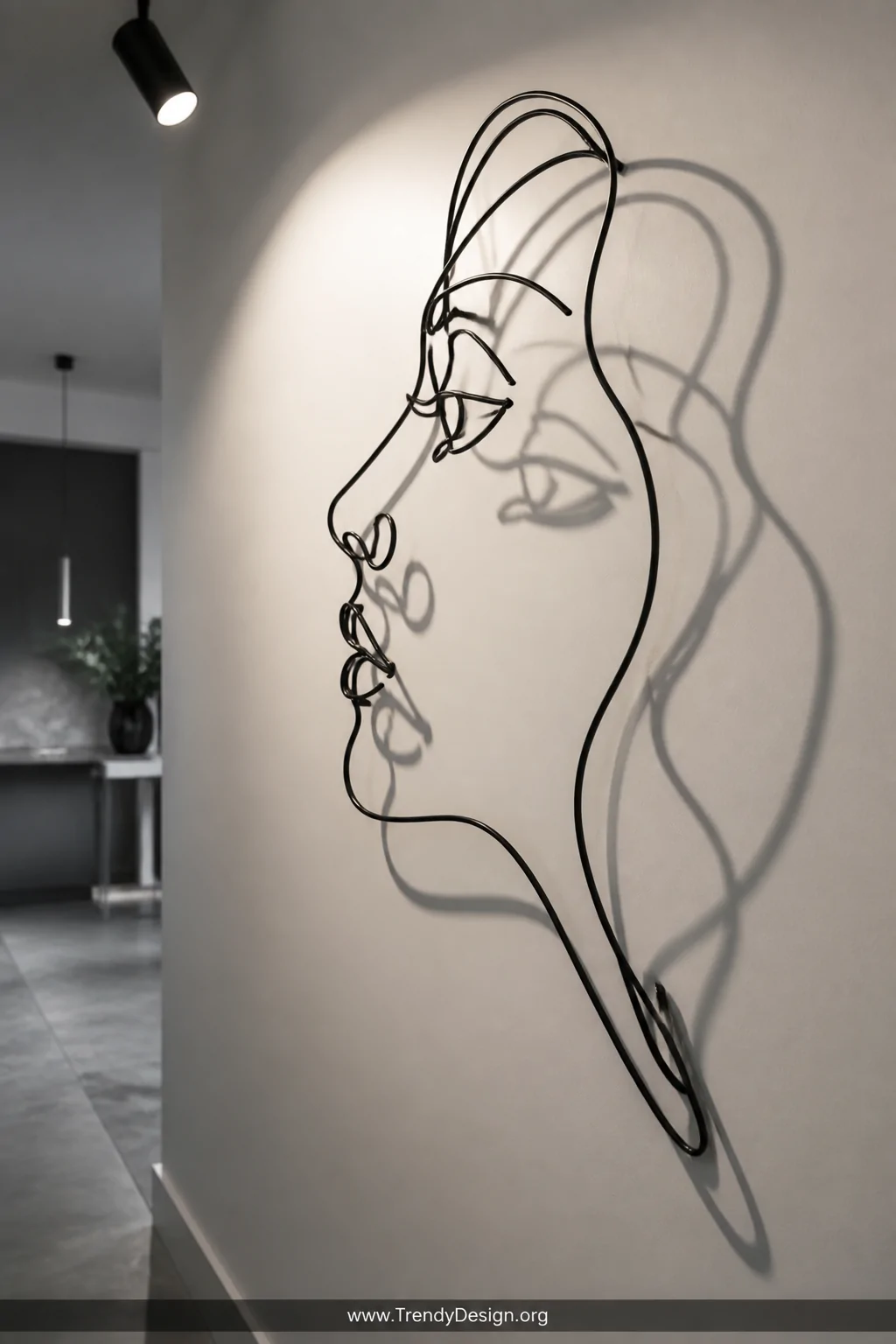 A closeup detail shot of a continuous-line wire sculpture portrait mounted against a smooth matte white wall, bent metal wire