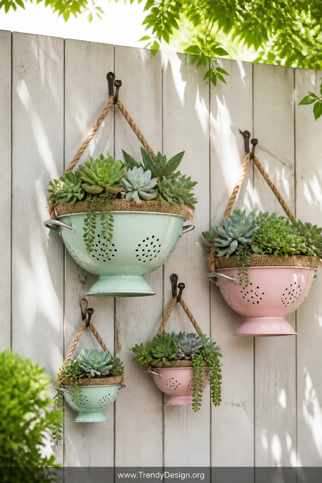 A medium shot of pastel mint and blush enamel colanders in graduated sizes mounted on a whitewashed wooden garden fence outdo