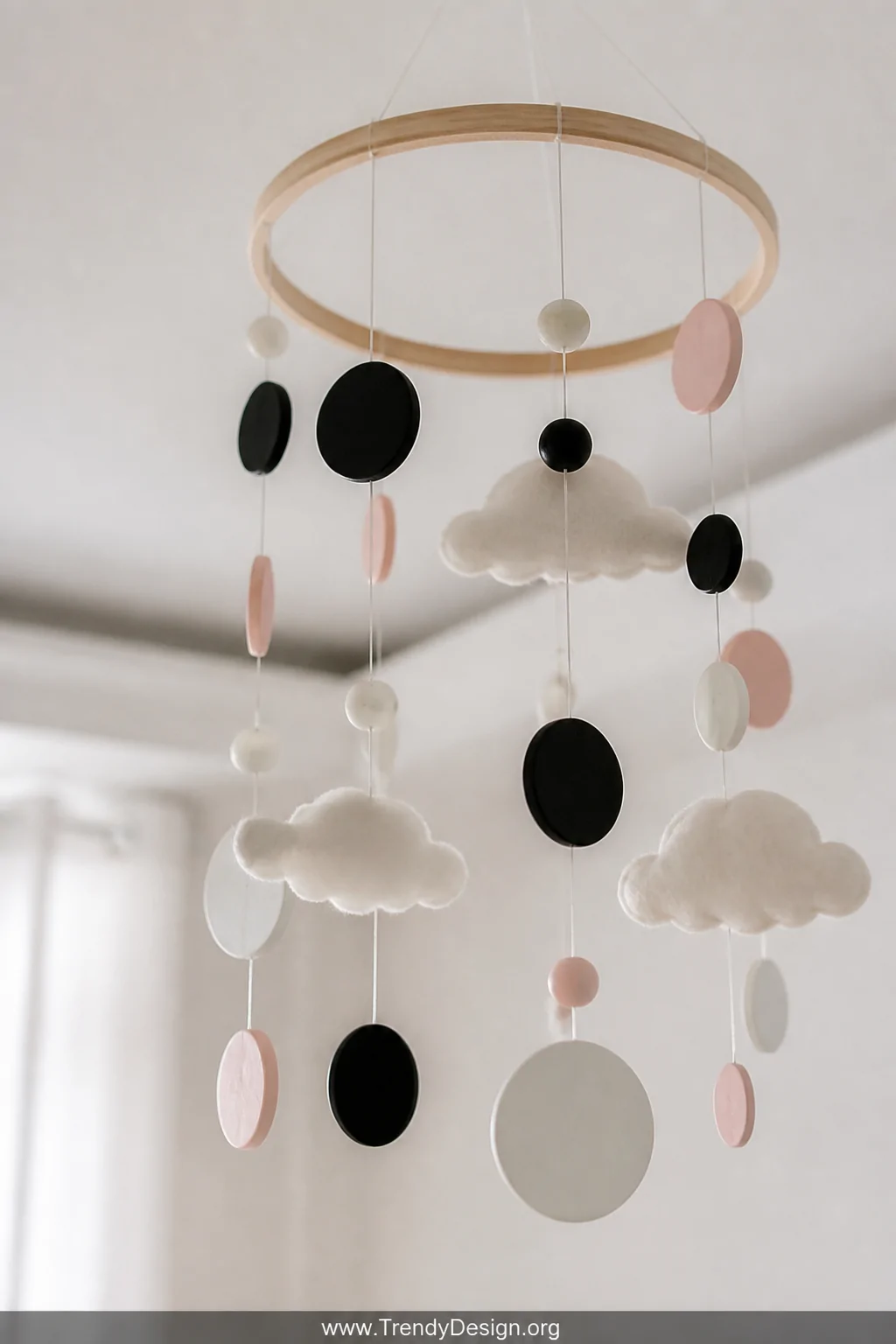 Close-up detail shot of a handmade nursery mobile hanging from a natural wooden hoop, featuring delicate felt cloud shapes, g