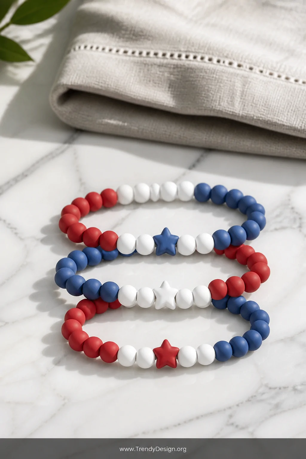 A close-up flat lay shot on a white marble surface of a neatly arranged clay bead bracelet in alternating red, white, and blu