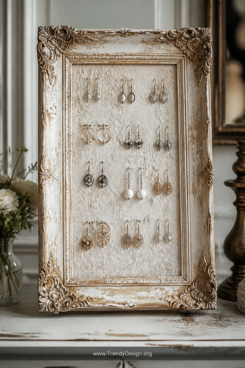 A medium shot of an ornate, paint-chipped vintage picture frame stretched with ivory lace fabric and hung with multiple pairs
