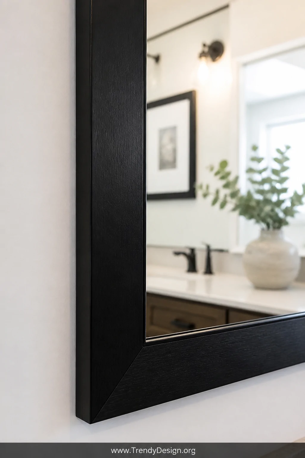 A close-up detail shot of a bathroom mirror with a freshly DIY-framed edge in dark black-painted wood trim, reflecting a soft