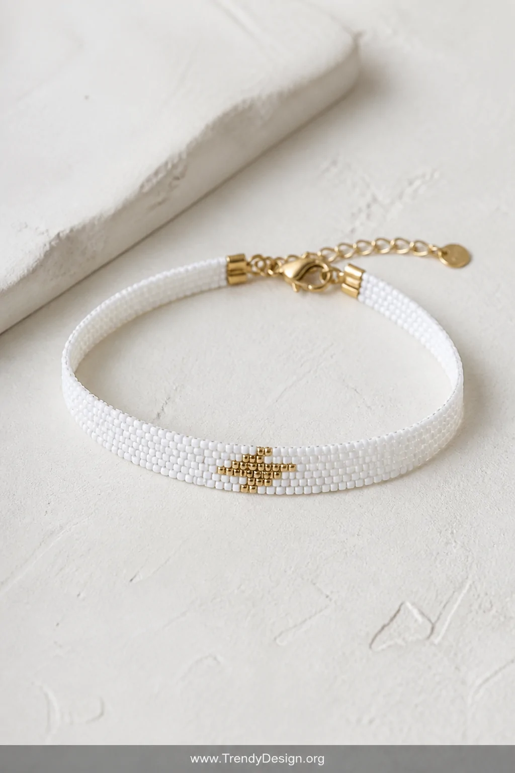A minimalist editorial closeup of a single seed bead loom bracelet resting on a smooth cream plaster surface, the bracelet fe