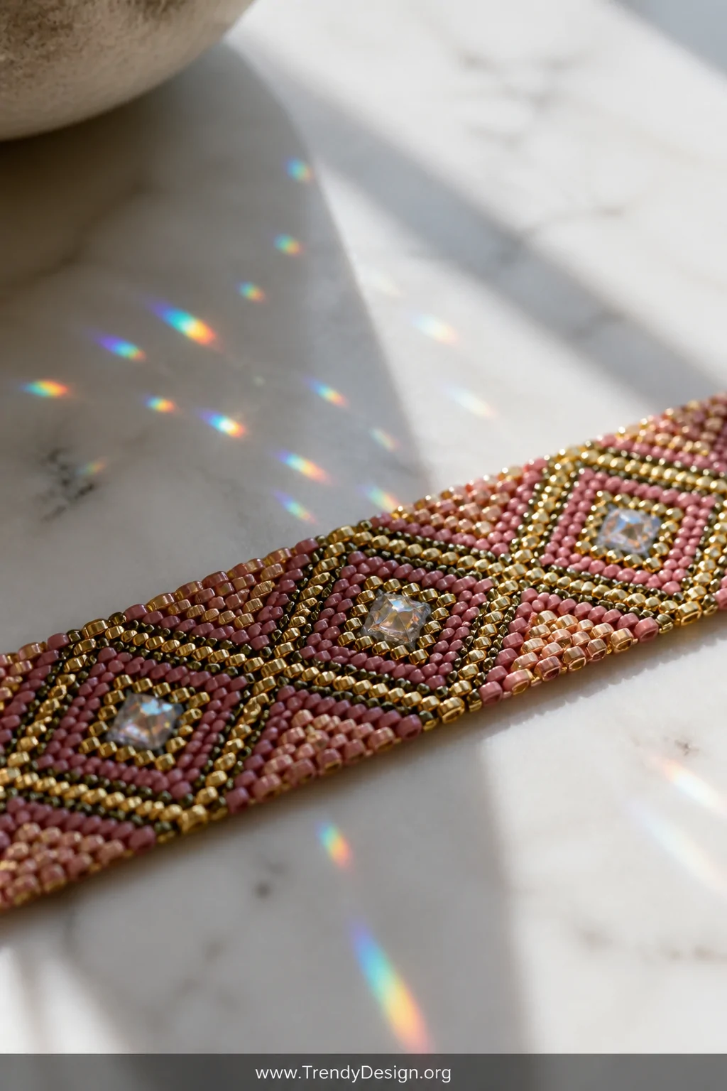 A detail macro shot of a seed bead loom bracelet laid across a white marble countertop, the bracelet showcasing a geometric d