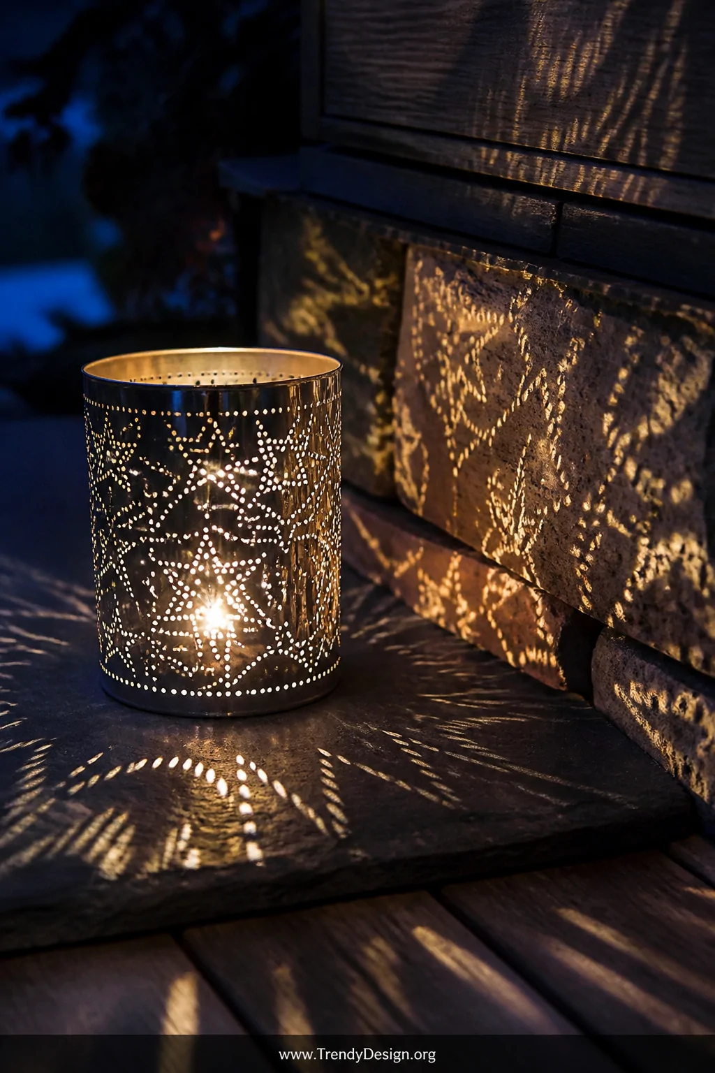 A close-up detail shot of a punched tin can lantern sitting on a dark slate patio surface, intricate star and geometric patte