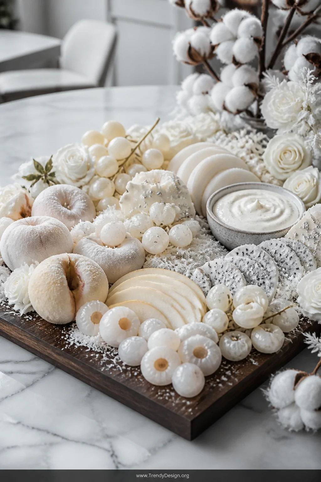 A wide elegant shot of a monochromatic winter wonderland fruit platter on a rich dark walnut wooden board set on a marble cou