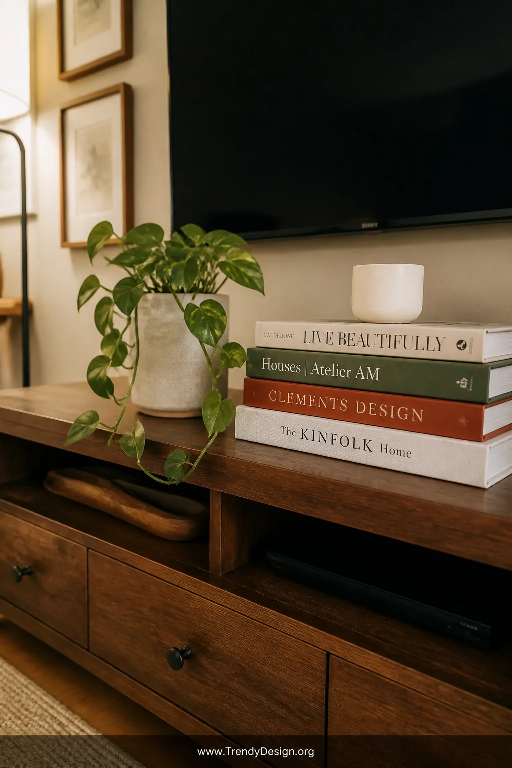 A wide shot of a styled living room media console with 4 large-format coffee table books stacked underneath a flatscreen TV, 