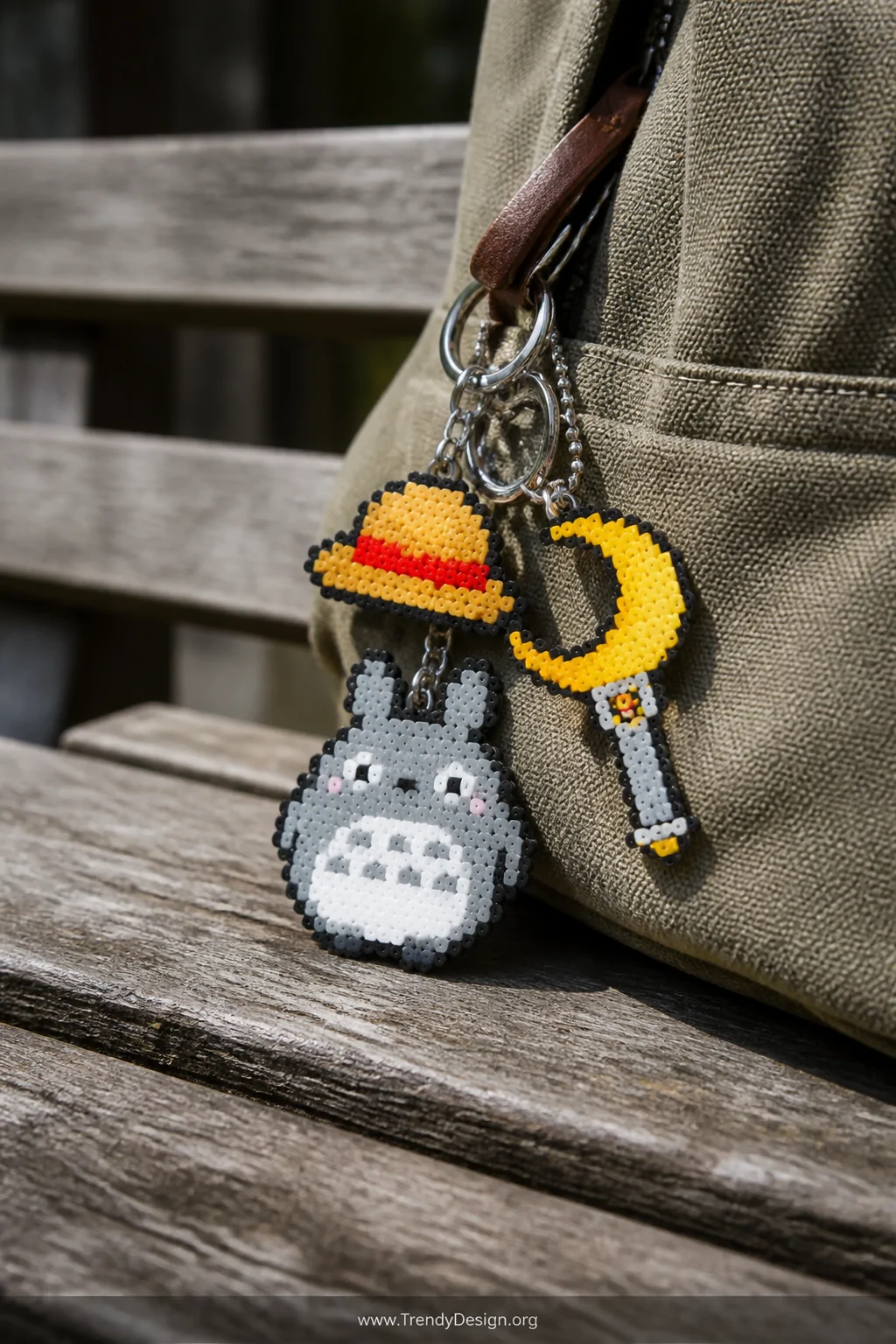 Close-up detail shot of a collection of miniature anime Perler bead keychains   a gray Totoro, a crescent moon wand in gold a