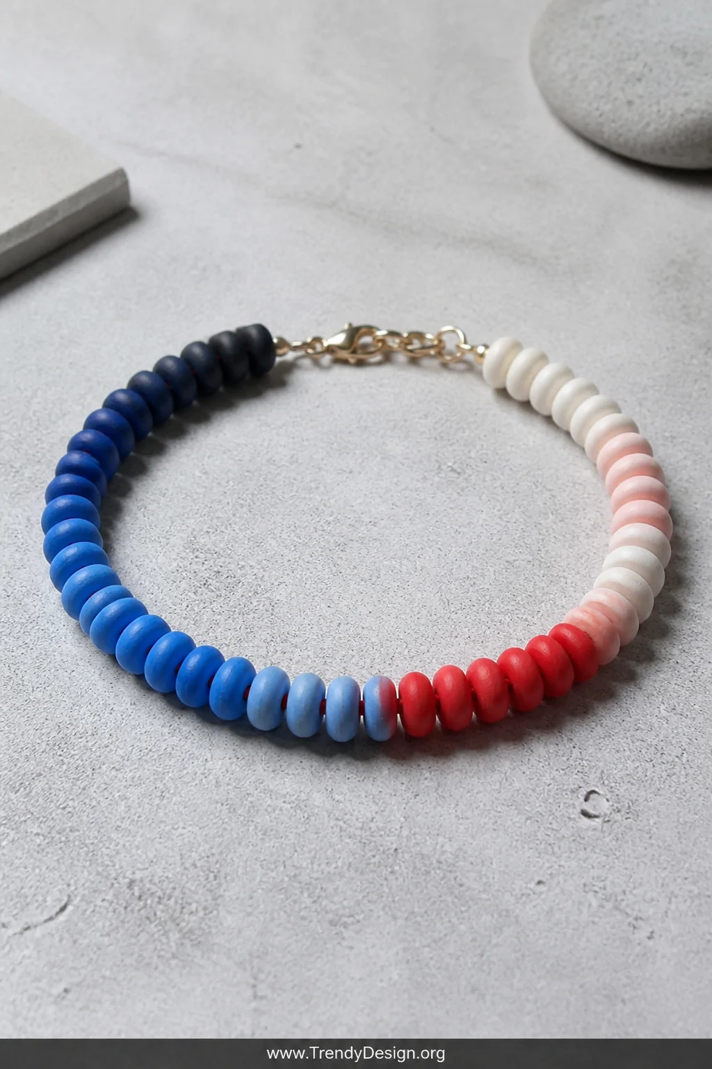 A wide flat lay shot on a light gray concrete surface of a clay bead bracelet displaying a stunning ombre gradient flowing fr