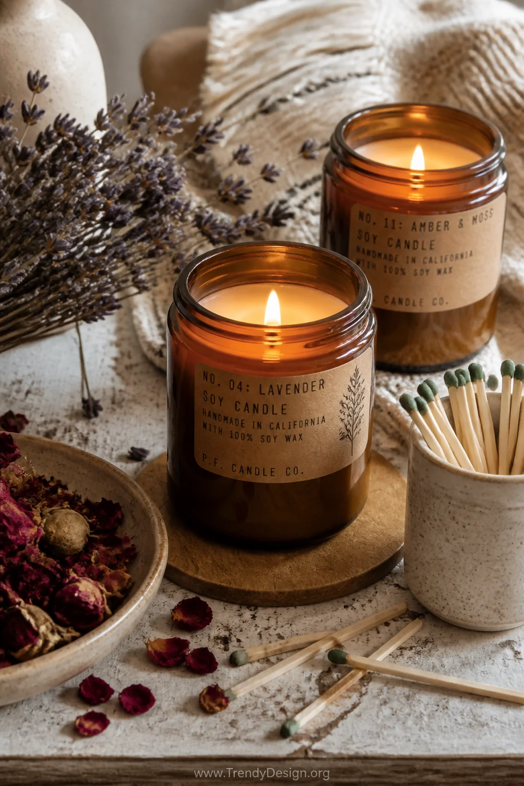 A cozy flat-lay detail shot of artisan soy candles in amber glass jars with kraft paper labels, surrounded by dried lavender 