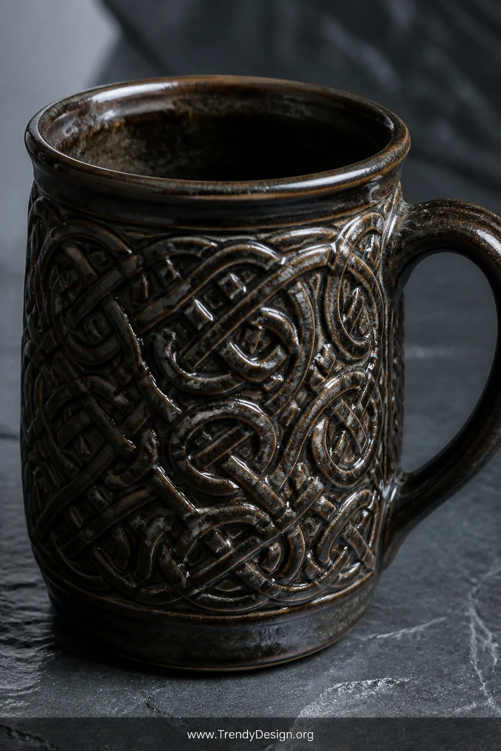 A closeup detail shot of a dark-glazed ceramic mug resting on a slate grey stone surface, its surface covered in precisely ca