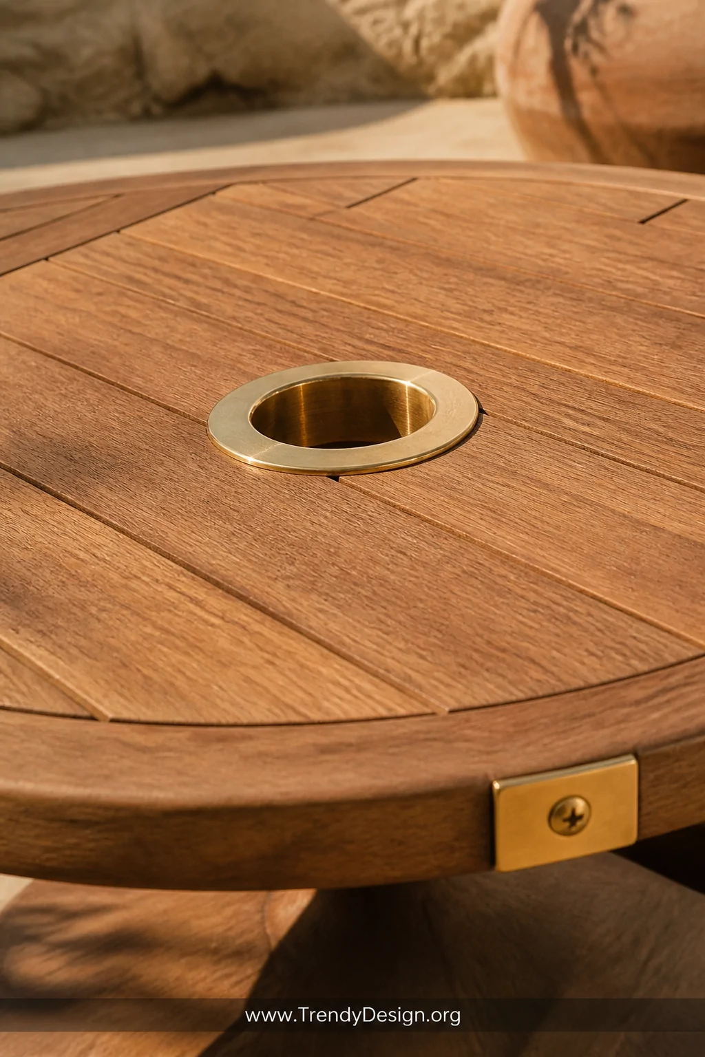 A close-up detail shot of a round patio table surface featuring a polished brass umbrella hole ring insert at center, warm Me