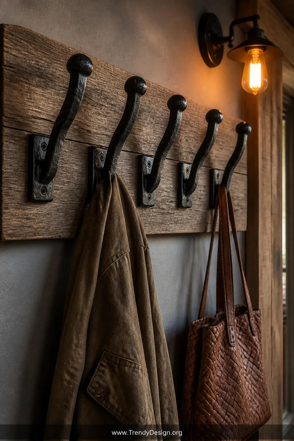 Medium shot of a rustic entryway wall featuring five hand-forged railroad spike hooks mounted in a staggered row on a wide ba