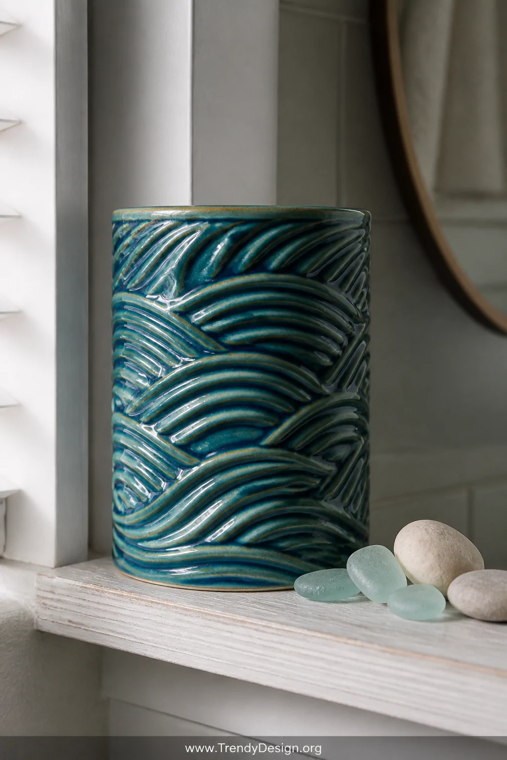 A closeup detail shot of a cylindrical ceramic vessel with flowing, overlapping wave carvings finished in a rich teal and oce