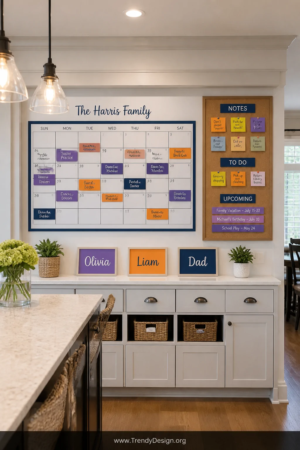 A wide shot of a family command center wall in a bright kitchen, featuring a large monthly wall calendar with appointments co