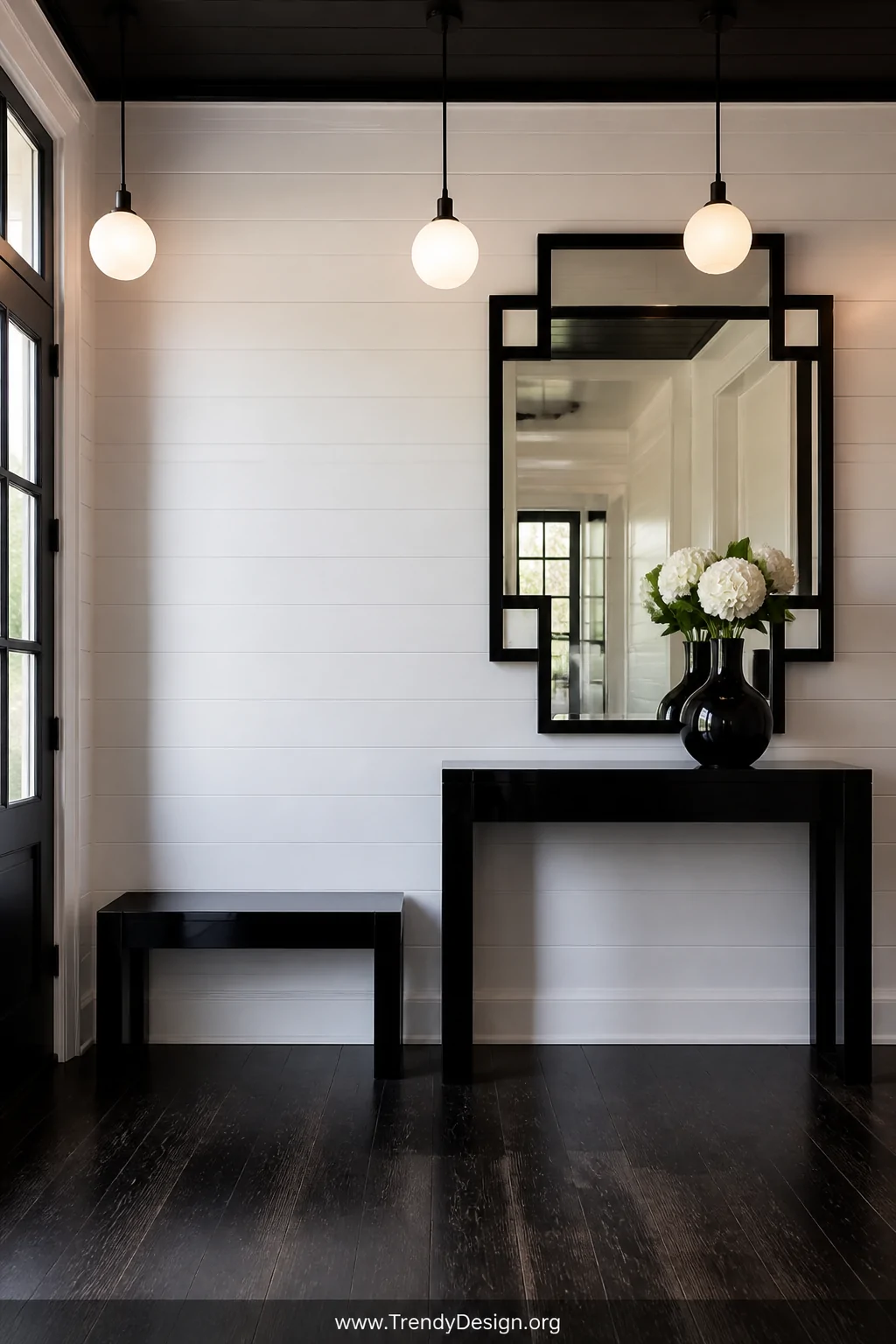 Wide shot of a minimalist entryway featuring a crisp white shiplap wall with a sleek black lacquered console table beneath a 