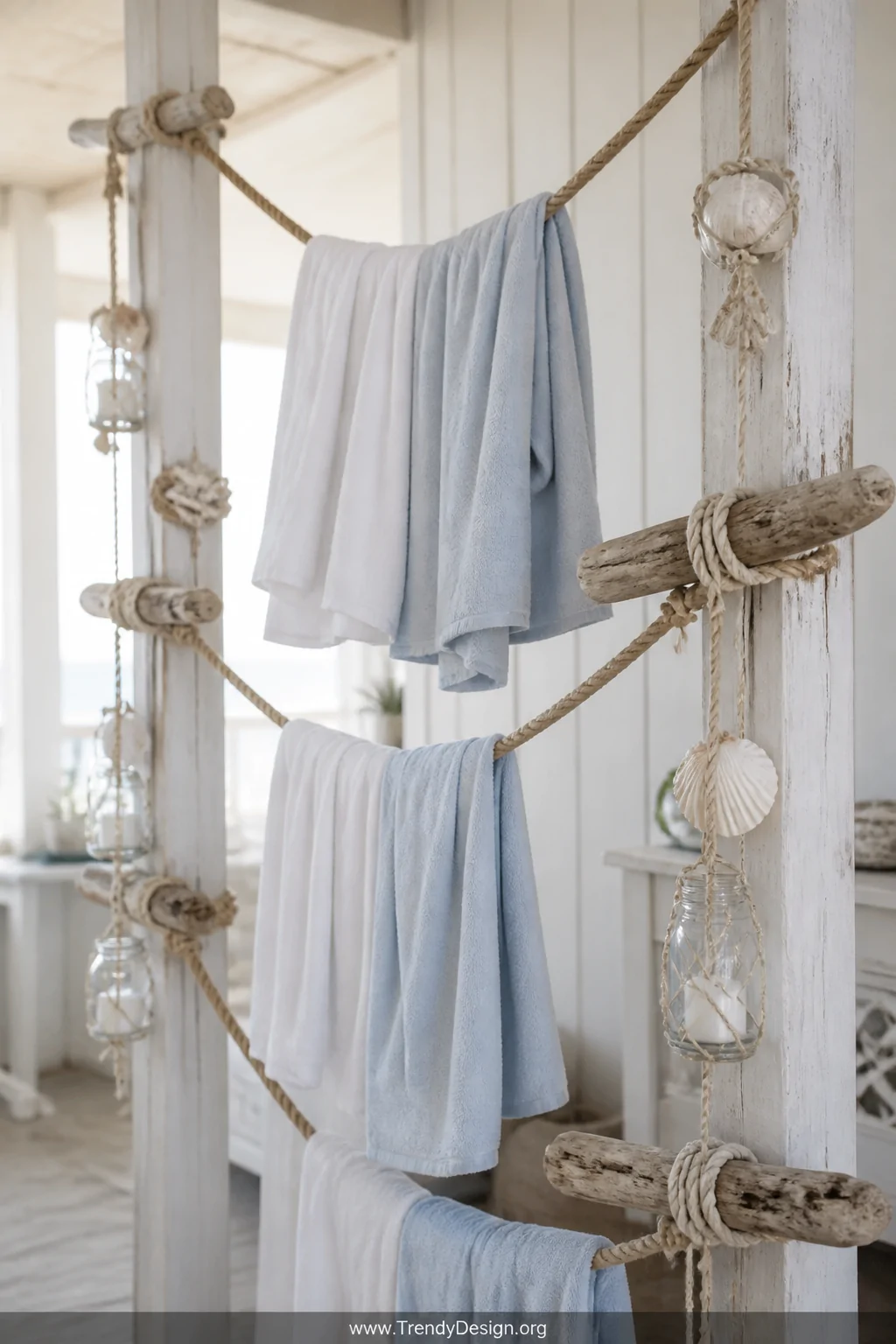 A detail shot of a coastal-style DIY rope towel display stretched between two whitewashed wooden posts, thick natural nautica