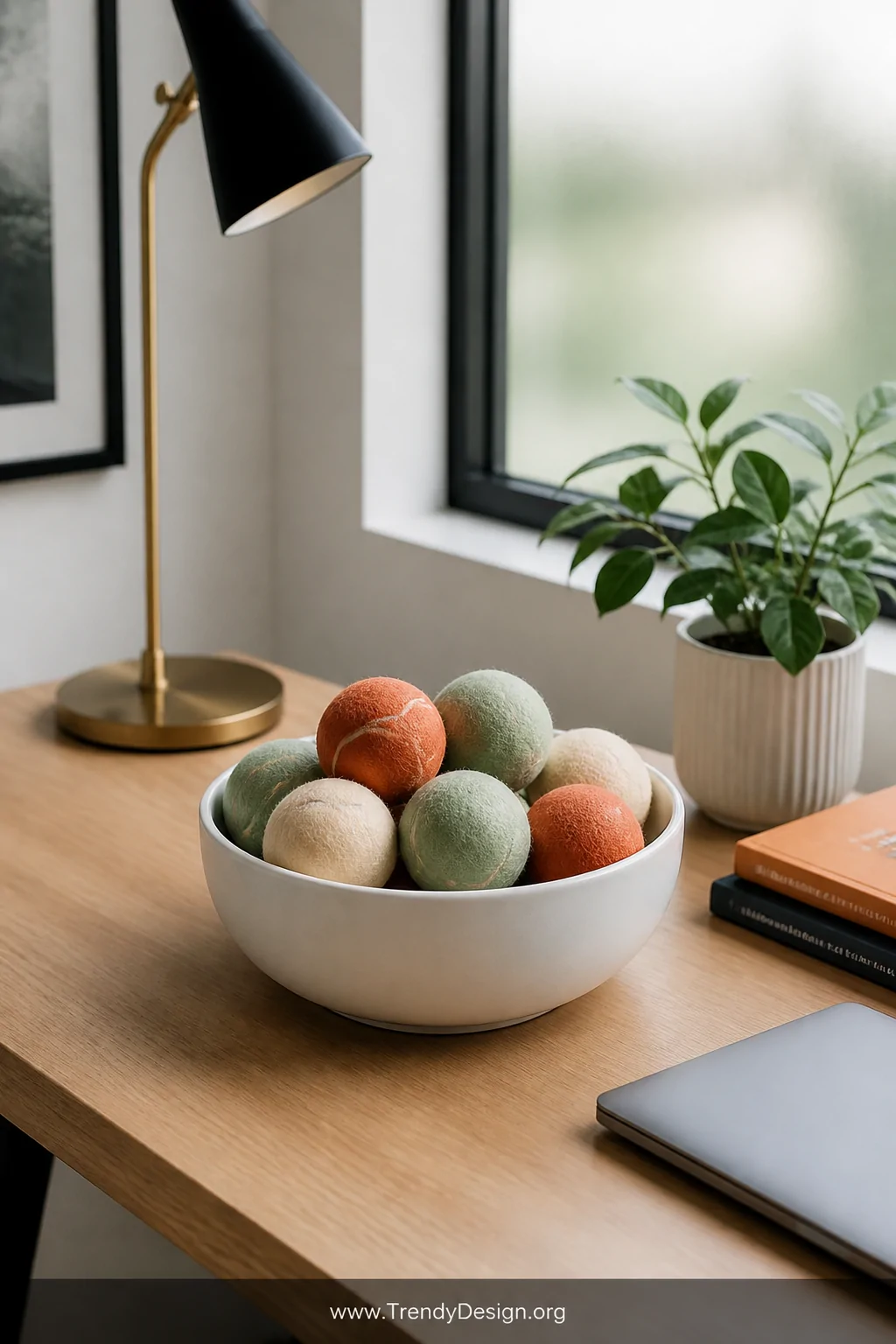 A medium shot of a tidy modern home desk with a light wood surface, featuring a round white ceramic bowl filled with neatly a