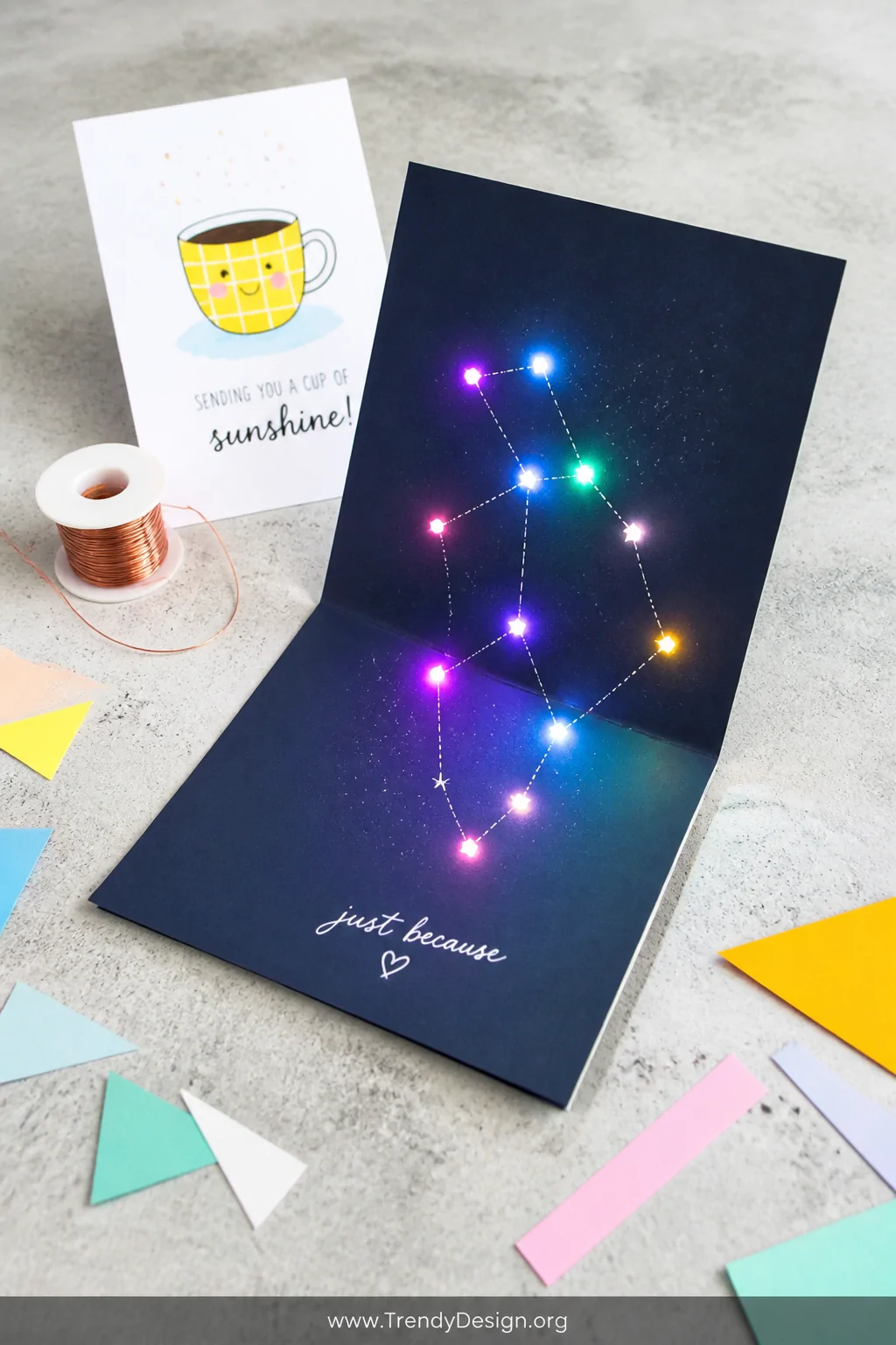 A wide, cheerful flat-lay shot on a light gray concrete surface featuring a playful just-because LED card opened to reveal a 