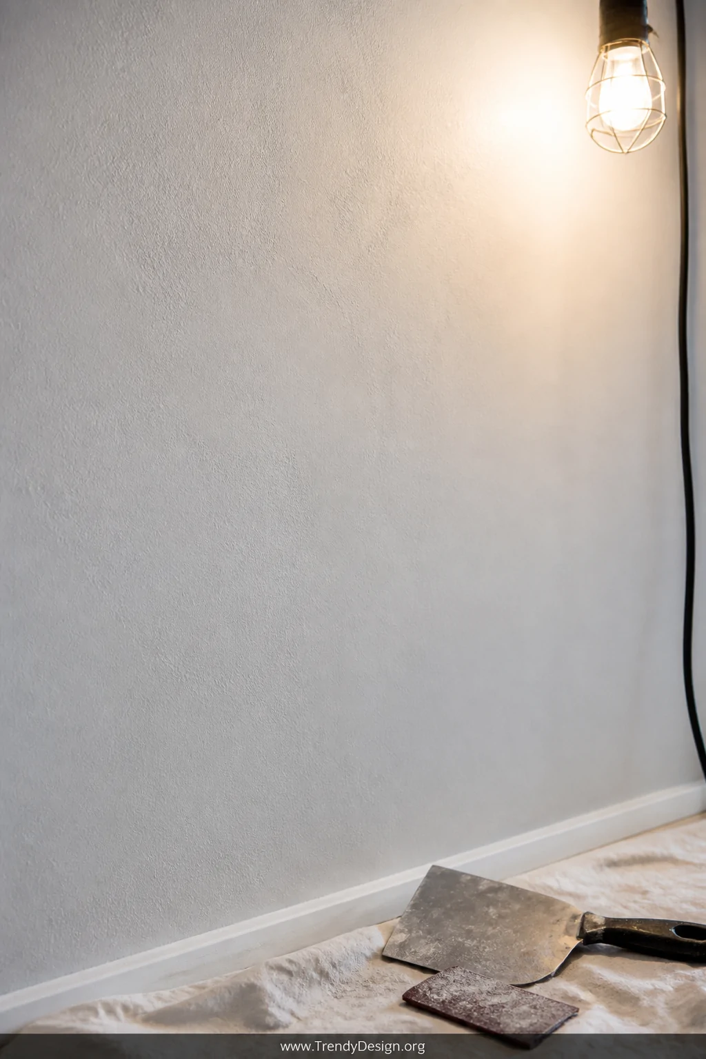 A smooth, freshly skim-coated wall surface in a neutral white room, a fine-sanded texture visible in the raking light from a 