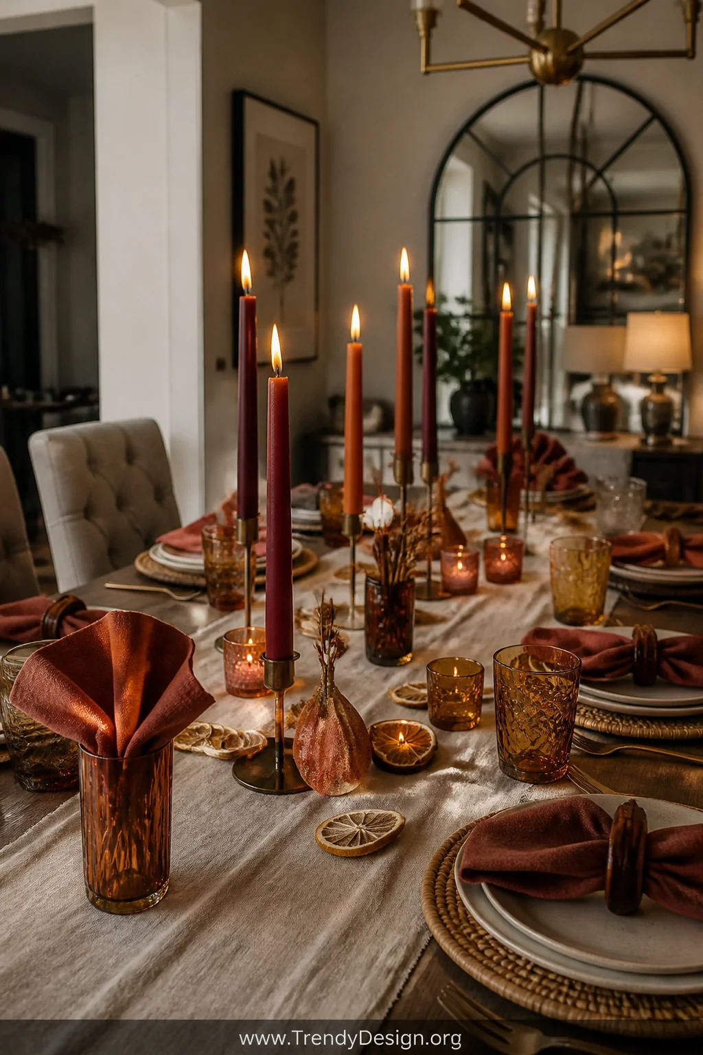 A wide shot of a fall dining table tablescape anchored by a set of complementary amber and rust-toned tumblers, layered over 