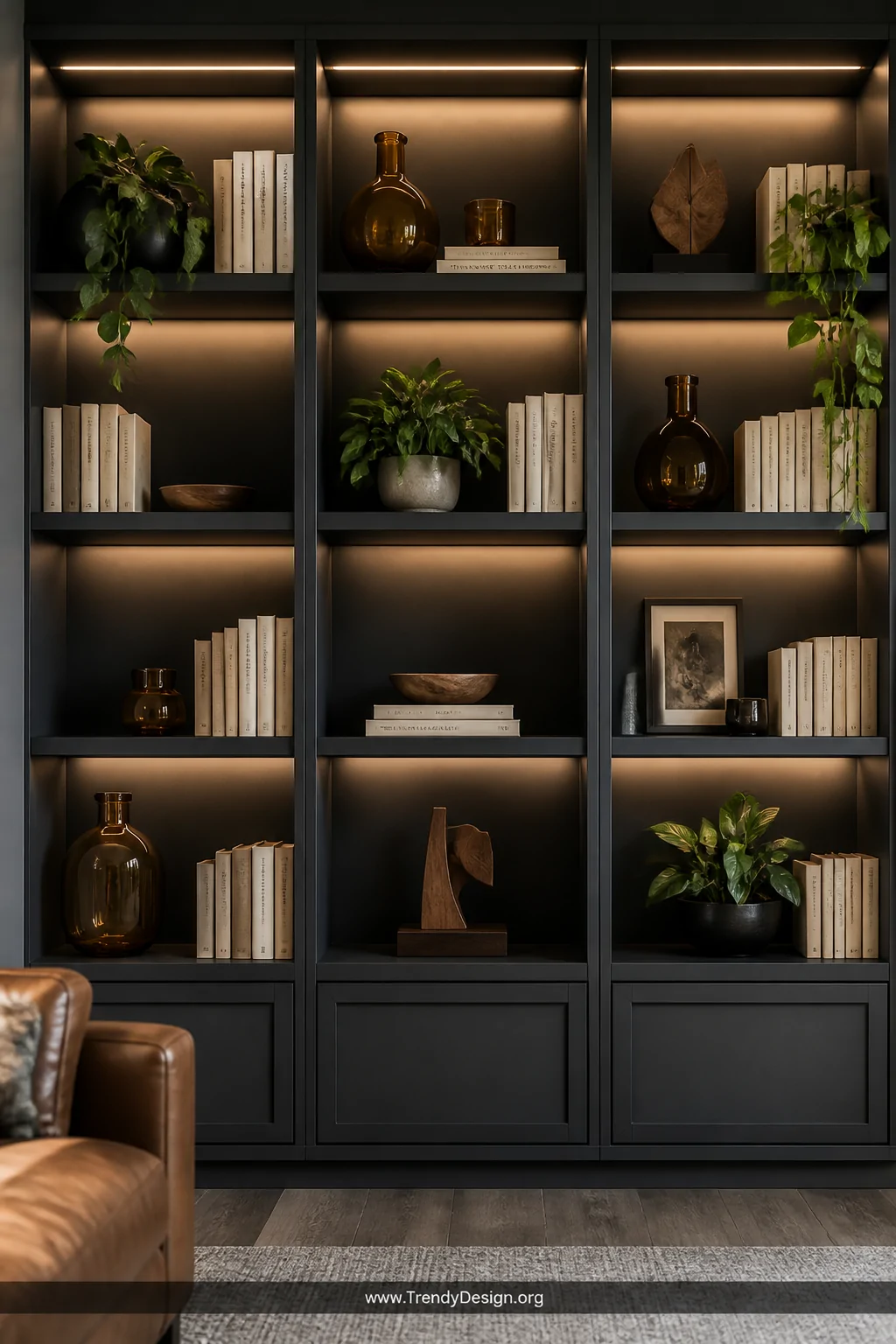 A detail-focused medium shot of a floor-to-ceiling dark charcoal bookcase styled with amber glass vases, small wooden sculptu