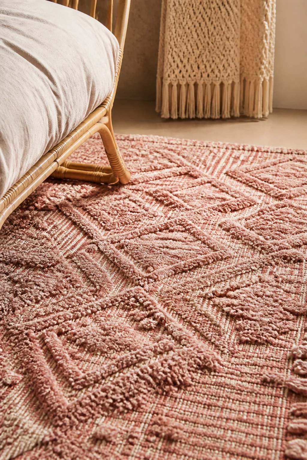 Close-up photorealistic detail shot of a textured pink boho rug with a high-low pile woven pattern, shot beside rattan furnit